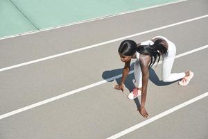 vista superior da bela jovem africana em pé na posição inicial na pista de corrida ao ar livre foto