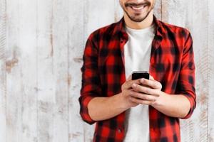 seu ajudante inteligente. foto recortada de jovem bonito segurando o celular e sorrindo em pé contra a parede de madeira