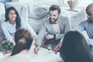 tomar decisões em conjunto. grupo de jovens empresários discutindo algo enquanto estão sentados juntos e apontando grande planta na mesa foto