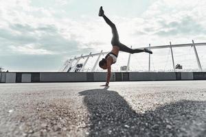 poder e equilíbrio. comprimento total da jovem moderna em roupas esportivas fazendo parada de mãos enquanto se exercita ao ar livre foto