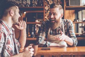 compartilhando boas notícias. barista e seu cliente discutindo algo com sorriso enquanto está sentado no balcão do bar no café foto