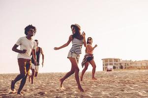 jovem e livre. grupo de jovens alegres correndo ao longo da praia e parecendo feliz foto