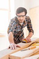 precisão e perfeição. concentrado jovem carpinteiro masculino lixando madeira em sua oficina foto