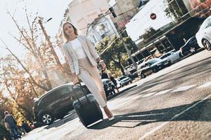 a caminho da reunião de negócios. comprimento total de jovem de terno puxando bagagem enquanto caminhava ao ar livre foto