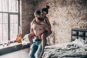 sempre felizes juntos. jovem casal se divertindo no quarto em casa enquanto homem sem camisa dando carona para sua namorada foto