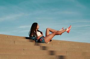 brincalhão. mulher jovem e atraente em roupas esportivas sorrindo enquanto está sentado nos degraus ao ar livre foto