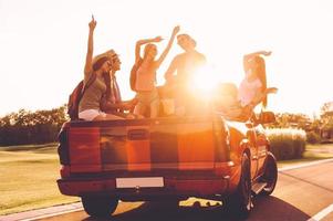 pronto para aventuras. grupo de jovens alegres dançando e tocando violão enquanto desfrutam de sua viagem na caminhonete juntos foto