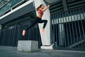 comprimento total de mulher jovem e atraente em roupas esportivas pairando em um salto em distância enquanto se exercita ao ar livre foto