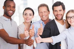 equipe de negócios feliz. grupo de empresários alegres em roupas casuais em pé perto um do outro e mostrando os polegares para cima foto