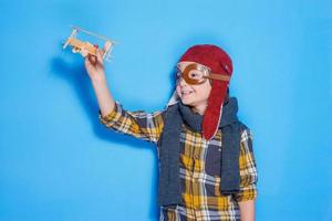 nas ondas da minha imaginação. menino feliz no capacete brincando com avião de brinquedo em pé contra um fundo azul foto