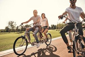 passando o dia despreocupado juntos. grupo de jovens felizes em roupas casuais sorrindo enquanto andam de bicicleta juntos ao ar livre foto