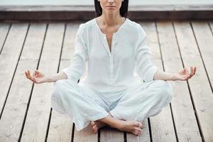 em paz e equilíbrio com o mundo. imagem recortada de mulher jovem e bonita em roupas brancas, sentado em posição de lótus e meditando ao ar livre foto