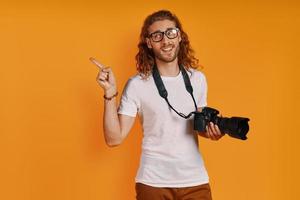 jovem feliz em roupas casuais, apontando o espaço da cópia e sorrindo em pé contra um fundo amarelo foto