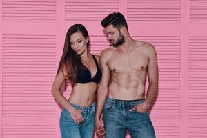 casal de jeans. lindo casal jovem de mãos dadas em pé contra um fundo rosa foto