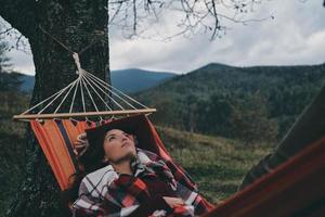 pensando... bela jovem deitada na rede enquanto relaxa no vale debaixo da árvore foto