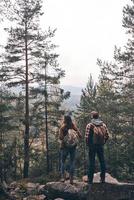 vista traseira de corpo inteiro do jovem casal admirando a vista enquanto caminhavam juntos na floresta foto