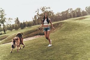 aproveitando o dia de verão. comprimento total de mulher jovem e bonita brincando com seu cachorro e sorrindo em pé ao ar livre foto