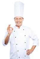 chef confiante. chef maduro confiante em uniforme branco, gesticulando sinal de ok e sorrindo em pé contra um fundo branco foto