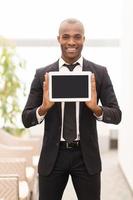 junte-se a uma era digital. alegre jovem africano em trajes formais, mostrando uma tela de tablet digital e sorrindo para a câmera foto