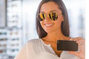 selfie na loja de óptica. bela jovem fazendo selfie e sorrindo em frente ao espelho na loja de óptica foto