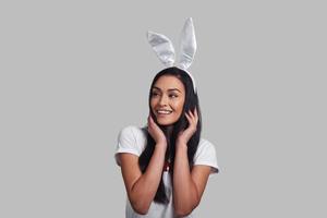 mais bonito do que qualquer coelho. mulher jovem e atraente em orelhas de coelho olhando para longe e sorrindo em pé contra um fundo cinza foto