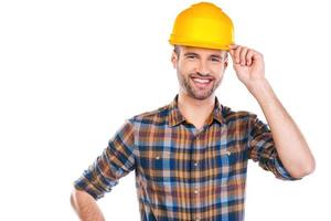 Pronto para trabalhar. confiante jovem carpinteiro masculino ajustando seu capacete e sorrindo em pé contra um fundo branco foto