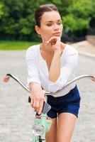 aproveitando seu tempo livre no parque. mulher jovem e atraente tomando café e olhando para longe enquanto caminhava com sua bicicleta no parque foto