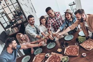 brinde à nossa amizade vista superior de jovens em roupas casuais brindando e sorrindo enquanto fazem um jantar dentro de casa foto