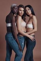 liberte sua fabulosidade. comprimento total de três mulheres jovens atraentes olhando para a câmera em pé contra um fundo marrom foto