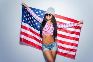 adolescente americano. bela jovem negra carregando a bandeira americana e sorrindo em pé contra um fundo cinza foto