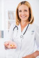 pílulas para torná-lo saudável. bela médica de uniforme branco segurando pílulas coloridas na palma da mão e sorrindo foto