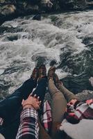 Juntos para sempre. close-up vista superior do jovem casal de mãos dadas enquanto está sentado nas rochas com o rio abaixo foto