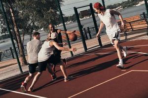 fazendo esforço. grupo de jovens em roupas esportivas jogando basquete enquanto passa o tempo ao ar livre foto