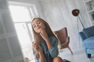 bela princesa. menina orgulhosa mantendo a mão no queixo e brincando com uma varinha mágica enquanto passa o tempo em casa foto