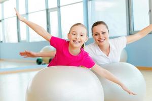 exercitar juntos é divertido. alegre mãe e filha se exercitando com bolas de fitness e olhando para a câmera foto