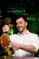 tem um pouco de cerveja alegre jovem barman servindo cerveja e desviando o olhar foto