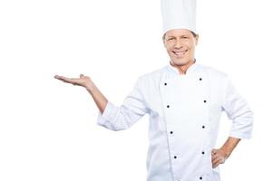 copie o espaço na mão. chef maduro confiante em uniforme branco, segurando o espaço da cópia na mão e sorrindo em pé contra um fundo branco foto