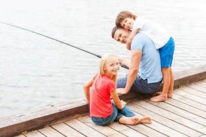 passando muito tempo com o pai. pai feliz pescando com seus filhos enquanto está sentado na margem do rio juntos foto