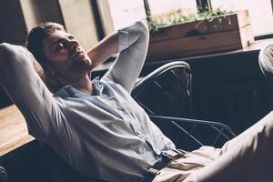 sentindo tão cansado. jovem bonito dormindo em seu local de trabalho no escritório, segurando as mãos atrás da cabeça foto