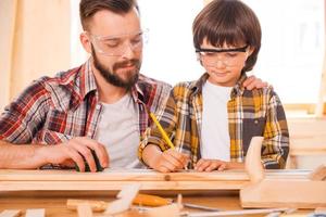 um dia você será um carpinteiro talentoso. concentrado jovem carpinteiro masculino ensinando seu filho a trabalhar com madeira em sua oficina foto