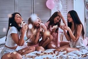 sabor maravilhoso. quatro mulheres bonitas de pijama comendo bolo enquanto fazem uma festa do pijama no quarto foto