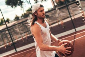 cheio de energia. jovem em roupas esportivas jogando basquete enquanto passa o tempo ao ar livre foto