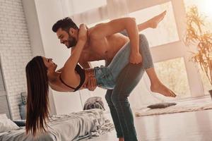 ficando loucos juntos. comprimento total do belo casal jovem abraçando e sorrindo enquanto dançava no quarto foto