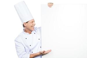 o melhor do chef. chef maduro confiante em uniforme branco, inclinando-se para o espaço da cópia e apontando-o em pé contra um fundo branco foto