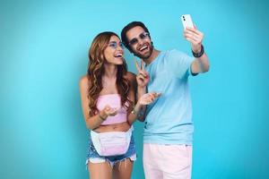 lindo jovem casal sorridente fazendo selfie em pé contra um fundo azul foto