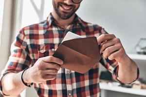 recebendo cartão. close-up de jovem abrindo o envelope e sorrindo em pé dentro de casa foto