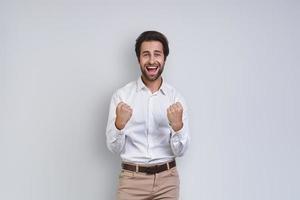 jovem feliz na camisa branca, gesticulando e olhando para a câmera em pé contra um fundo cinza foto