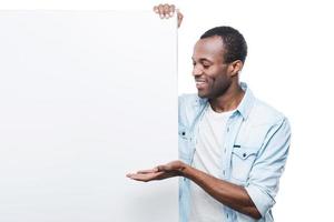 anunciando seu produto. belo jovem negro apontando e inclinando-se para o espaço de cópia em pé contra um fundo branco foto