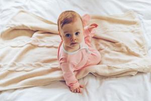 bonitinha na cama. vista superior menina olhando para a câmera enquanto está sentado no cobertor na cama foto