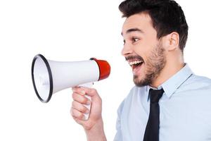 anunciando boas novas. Vista lateral do jovem feliz de camisa e gravata segurando o megafone e gritando em pé contra um fundo branco foto